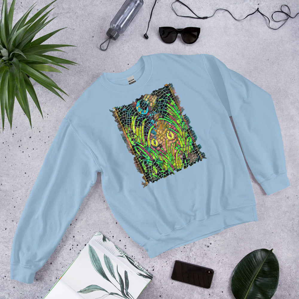 Light blue unisex sweatshirt featuring “Midnight Watcher” artwork in Amber Collection mosaic style (glowing yellow eyes in green grass under a crescent moon)