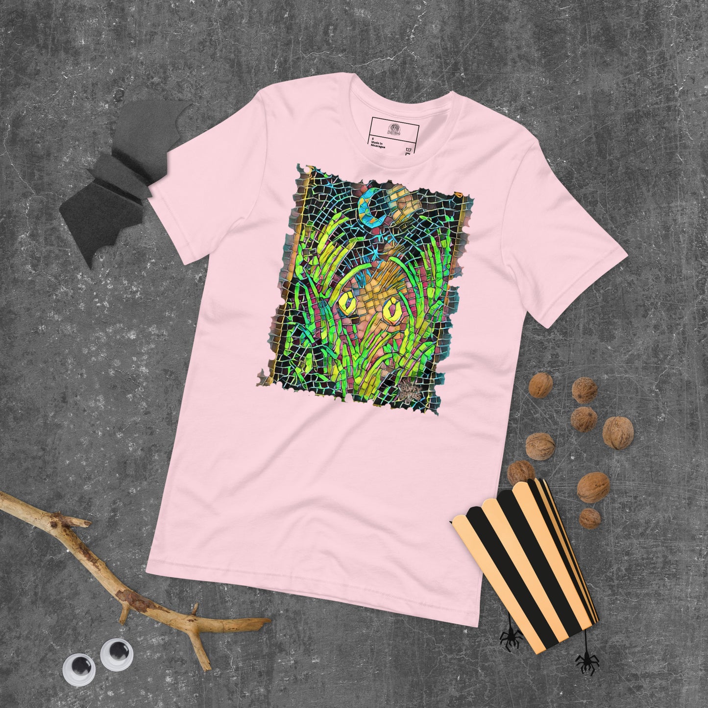 Soft pink unisex t-shirt featuring “Midnight Watcher” artwork in Amber Collection mosaic style (glowing yellow eyes in green grass under a crescent moon)