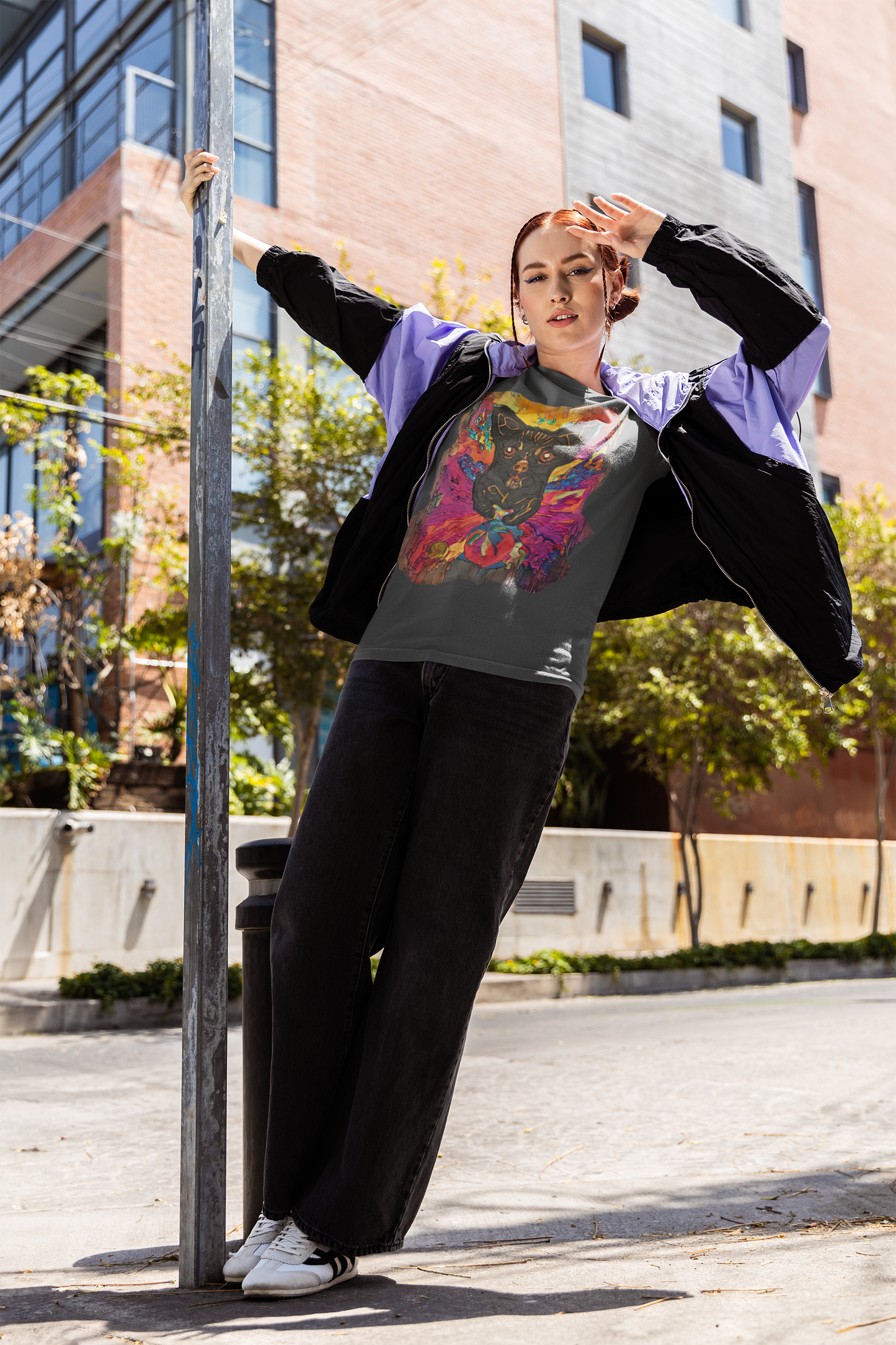 Person wearing a colorful graphic t-shirt and black jacket outdoors with buildings in the background