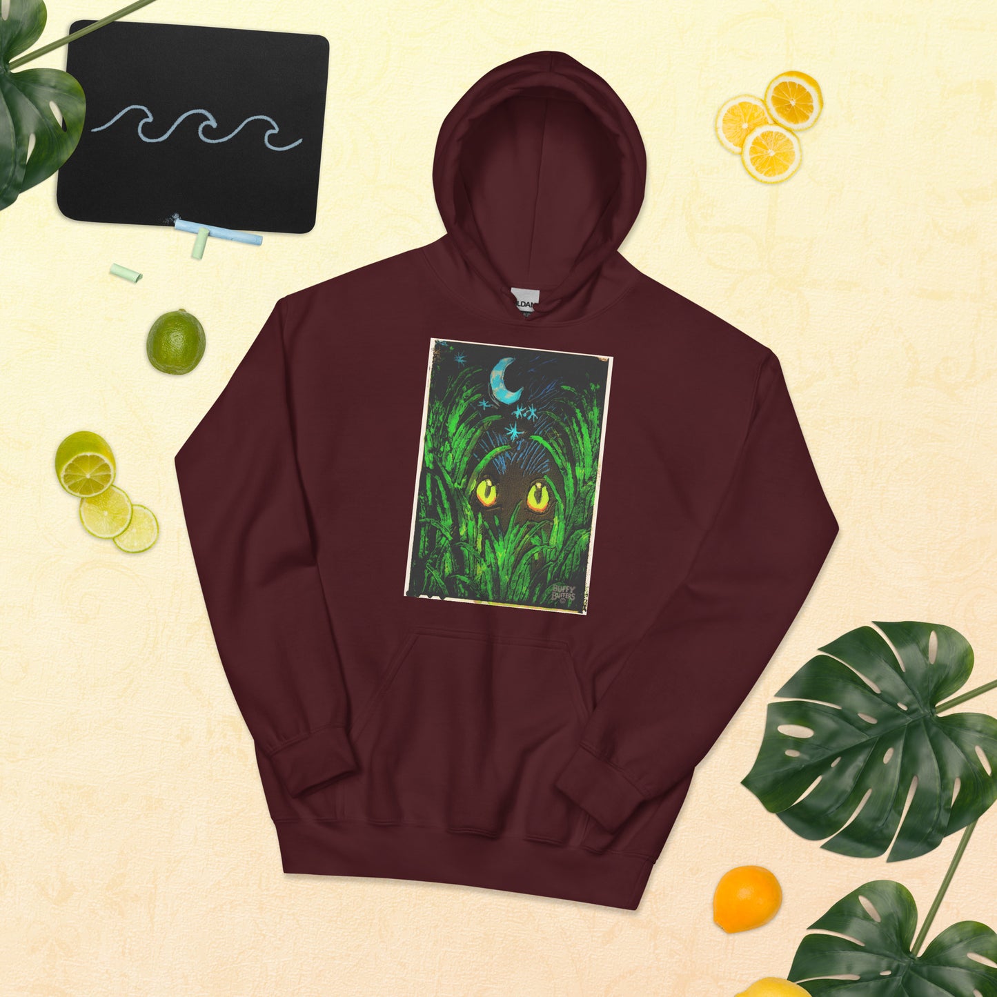 Maroon unisex hoodie featuring "Midnight Watcher" artwork – glowing yellow eyes in green grass under a crescent moon (Canva Collection)