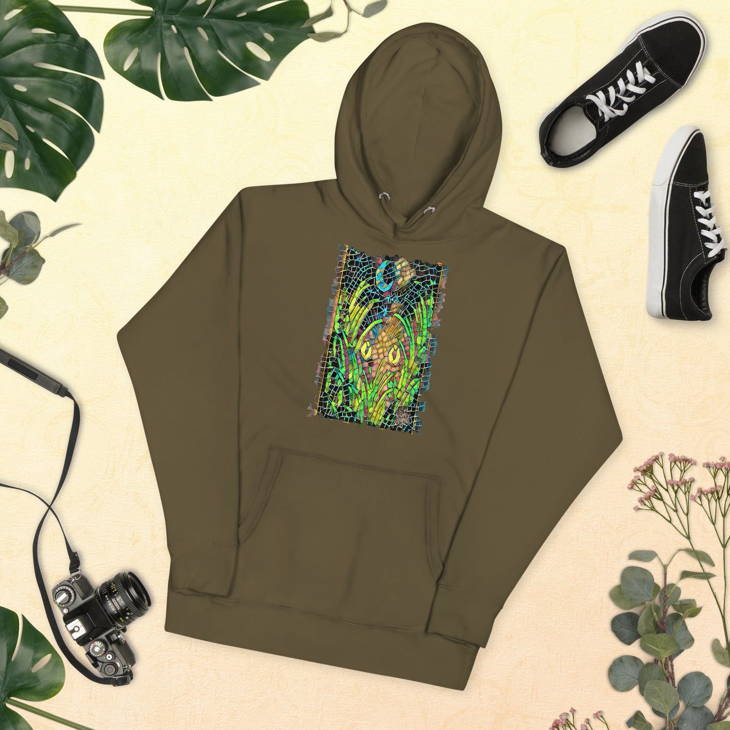 Military green unisex hoodie featuring “Midnight Watcher” artwork in Amber Collection mosaic style (glowing yellow eyes in green grass under a crescent moon)