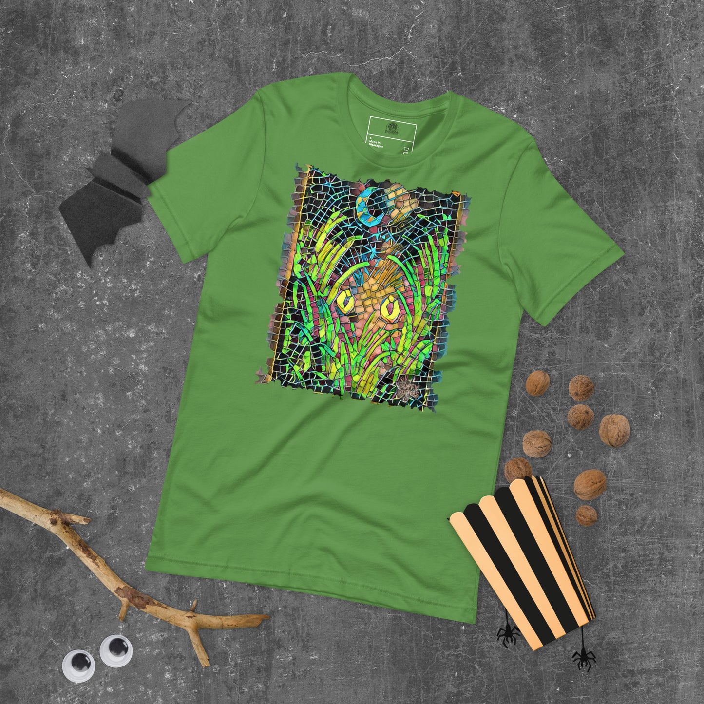 Leaf green unisex t-shirt featuring “Midnight Watcher” artwork in Amber Collection mosaic style (glowing yellow eyes in green grass under a crescent moon)