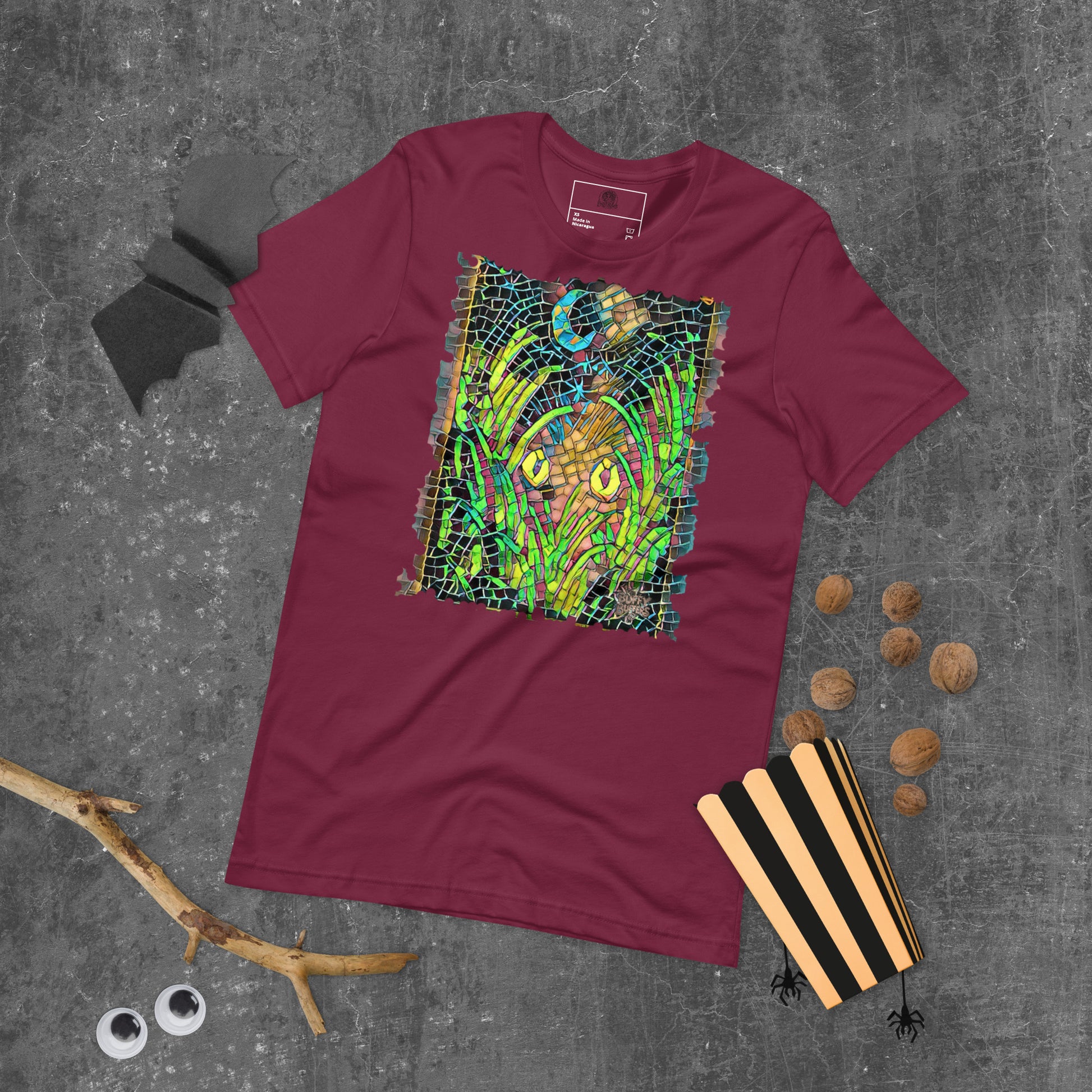 Maroon unisex t-shirt featuring “Midnight Watcher” artwork in Amber Collection mosaic style (glowing yellow eyes in green grass under a crescent moon)