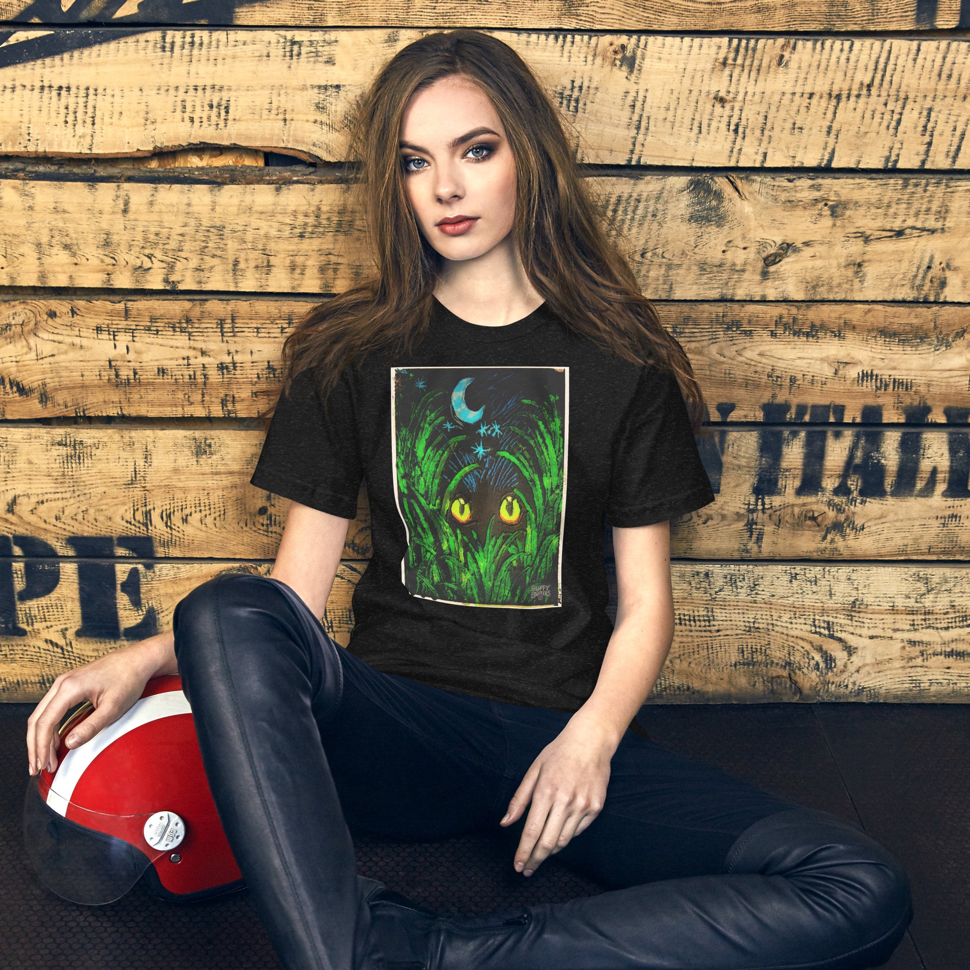 Model wearing black heather unisex t-shirt featuring "Midnight Watcher" artwork – glowing yellow eyes in green grass under a crescent moon (Canva Collection)