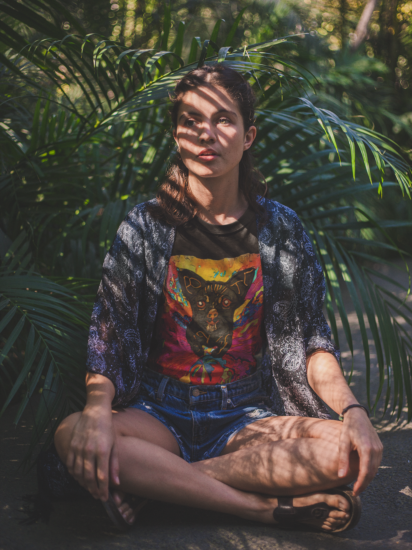 Person sitting among tropical plants wearing a colorful graphic t-shirt.
